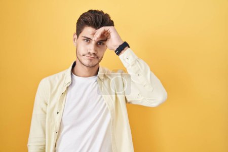 Photo for Young hispanic man standing over yellow background worried and stressed about a problem with hand on forehead, nervous and anxious for crisis - Royalty Free Image