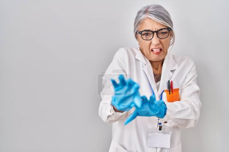 Photo for Middle age woman with grey hair wearing scientist robe disgusted expression, displeased and fearful doing disgust face because aversion reaction. with hands raised - Royalty Free Image