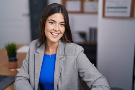 Photo for Young beautiful hispanic woman business worker smiling confident sitting on table at office - Royalty Free Image