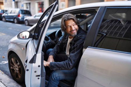 Foto de Hombre de mediana edad sonriendo confiado abriendo la puerta del coche en la calle - Imagen libre de derechos