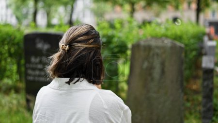 Foto de Hermosa joven hispana rezando y llorando junto a una lápida en el cementerio - Imagen libre de derechos