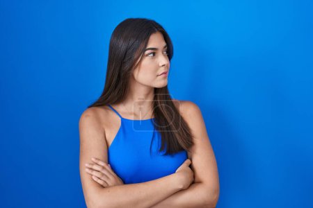 Téléchargez les photos : Femme hispanique debout sur fond bleu regardant sur le côté avec les bras croisés convaincu et confiant - en image libre de droit