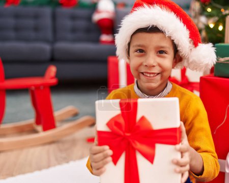 Foto de Adorable niño hispano sosteniendo regalo de Navidad sentado en el suelo en casa - Imagen libre de derechos