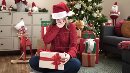 Foto de Joven mujer rubia desempacar regalo sentado en el suelo por el árbol de Navidad en casa - Imagen libre de derechos
