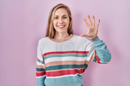 Téléchargez les photos : Jeune femme blonde debout sur fond rose montrant et pointant vers le haut avec les doigts numéro cinq tout en souriant confiant et heureux. - en image libre de droit