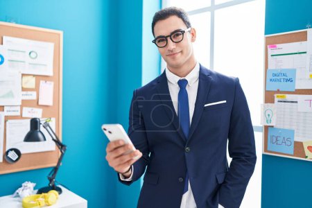 Photo for Young hispanic man business worker smiling confident using smartphone at office - Royalty Free Image