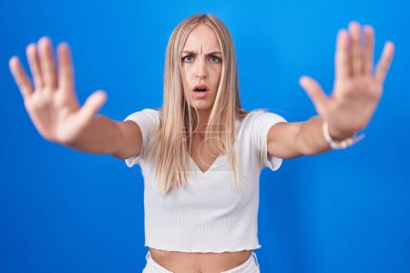 Photo for Young caucasian woman standing over blue background doing stop gesture with hands palms, angry and frustration expression - Royalty Free Image