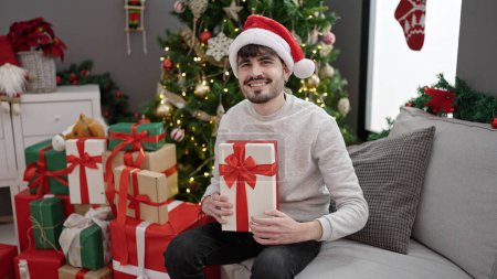 Photo for Young hispanic man smiling confident holding christmas gift at home - Royalty Free Image