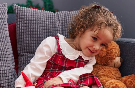 Téléchargez les photos : Adorable bambin hispanique souriant assis sur un canapé avec décoration de Noël à la maison - en image libre de droit
