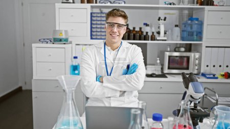 Foto de Radiante joven científico caucásico, sentado con los brazos cruzados en el laboratorio, inmerso en la investigación médica de alta tecnología - Imagen libre de derechos