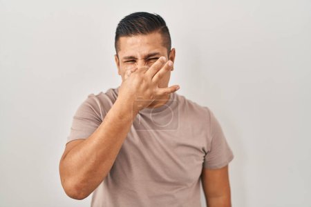 Photo for Hispanic young man standing over white background smelling something stinky and disgusting, intolerable smell, holding breath with fingers on nose. bad smell - Royalty Free Image