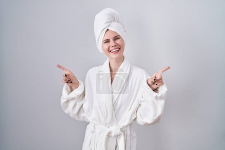 Téléchargez les photos : Femme caucasienne blonde portant un peignoir souriant confiant pointant avec les doigts vers différentes directions. espace de copie pour la publicité - en image libre de droit