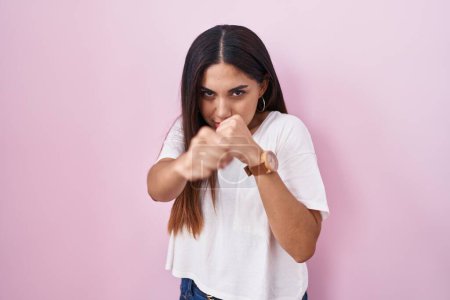 Téléchargez les photos : Jeune femme arabe debout sur fond rose coups de poing poing pour se battre, attaque agressive et en colère, menace et violence - en image libre de droit