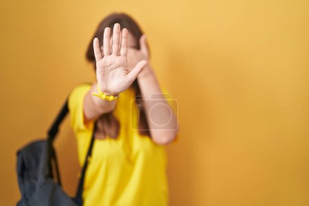 Photo for Young caucasian woman wearing student backpack over yellow background covering eyes with hands and doing stop gesture with sad and fear expression. embarrassed and negative concept. - Royalty Free Image