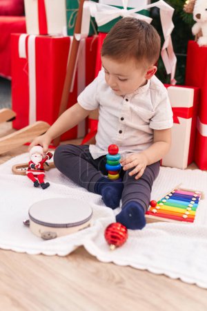 Foto de Adorable niño hispano jugando con juguetes sentados en el suelo por regalos de Navidad en casa - Imagen libre de derechos