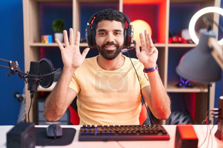 Téléchargez les photos : Homme hispanique avec barbe jouer à des jeux vidéo avec écouteurs montrant et pointant vers le haut avec les doigts numéro neuf tout en souriant confiant et heureux. - en image libre de droit