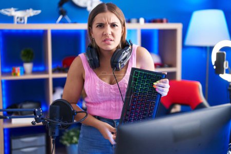 Photo for Young blonde woman playing video games holding keyboard clueless and confused expression. doubt concept. - Royalty Free Image