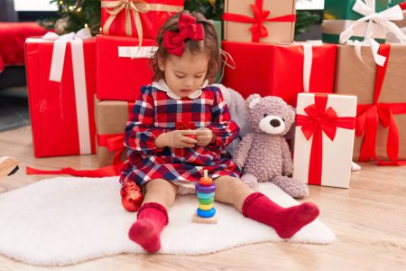 Téléchargez les photos : Adorable blonde tout-petit tenant jouet assis près de l'arbre de Noël à la maison - en image libre de droit