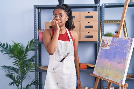 Téléchargez les photos : Jeune afro-américain avec des tresses au studio d'art peinture sur toile à l'air stressé et nerveux avec les mains sur les ongles mordants de la bouche. problème d'anxiété. - en image libre de droit