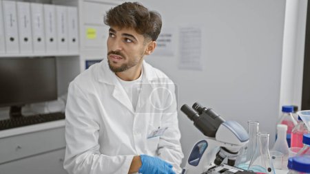 Photo for Handsome, young arabian scientist in distress, upset in laboratory over unsettling medical discovery using microscope - Royalty Free Image