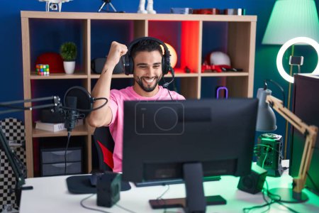 Photo for Young arab man streamer playing video game with winner expression at gaming room - Royalty Free Image