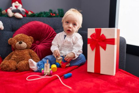 Foto de Adorable niño rubio jugando con el tren de madera sentado en el sofá por la decoración de Navidad en casa - Imagen libre de derechos