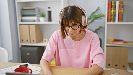 Photo for Radiant young hispanic businesswoman, exuding confidence, lost in music at her office desk, brings positivity to the indoor workspace with her radiant smile - Royalty Free Image