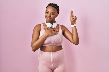 Photo for African american woman with braids wearing sportswear and headphones smiling swearing with hand on chest and fingers up, making a loyalty promise oath - Royalty Free Image