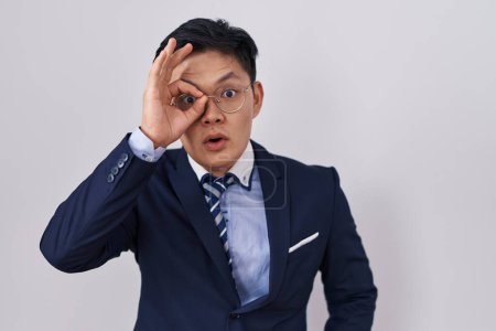 Téléchargez les photos : Jeune homme asiatique portant un costume d'affaires et une cravate faisant un geste correct choqué par le visage surpris, les yeux regardant à travers les doigts. expression incrédule. - en image libre de droit
