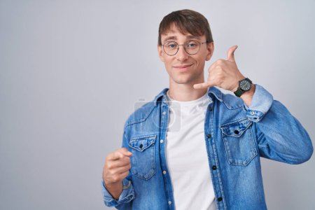 Photo for Caucasian blond man standing wearing glasses smiling doing talking on the telephone gesture and pointing to you. call me. - Royalty Free Image