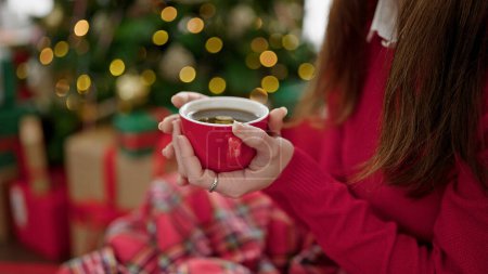 Photo for Young hispanic woman holding cup of coffee celebrating christmas at home - Royalty Free Image