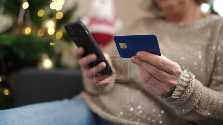 Téléchargez les photos : Femme du Moyen Âge avec les cheveux gris faire des achats en ligne de Noël avec smartphone à la maison - en image libre de droit