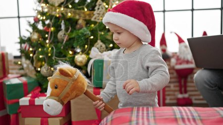 Photo for Caucasian toddler playing with christmas present rocking horse toy at home - Royalty Free Image