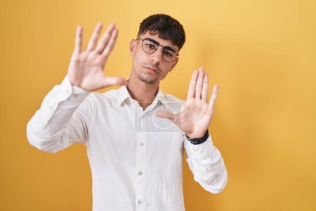 Téléchargez les photos : Young hispanic man standing over yellow background doing frame using hands palms and fingers, camera perspective - en image libre de droit