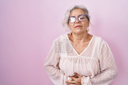Foto de Mujer de mediana edad con el pelo gris de pie sobre fondo rosa con la mano en el estómago porque la indigestión, la enfermedad dolorosa sensación de malestar. concepto ache. - Imagen libre de derechos
