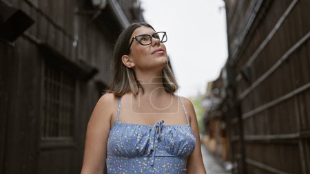 Photo for Cheerful hispanic woman posing with joy, glasses glinting, standing amidst traditional kyoto streets, bewitched by japanese architecture, her beautiful smile radiating confidence. - Royalty Free Image