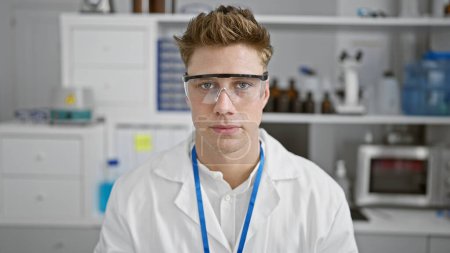 Téléchargez les photos : Sérieux jeune homme caucasien scientifique, grand et beau, portant des lunettes de sécurité, profondément concentré dans son travail de laboratoire - en image libre de droit