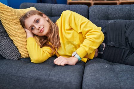 Téléchargez les photos : Jeune femme blonde souriante confiante allongée sur un canapé à la maison - en image libre de droit
