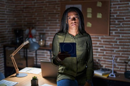 Photo for Young african american with braids working at the office at night relaxed with serious expression on face. simple and natural looking at the camera. - Royalty Free Image