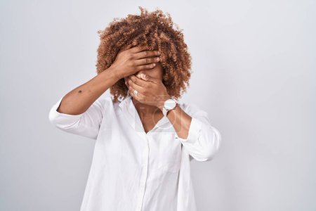 Photo for Young hispanic woman with curly hair standing over white background covering eyes and mouth with hands, surprised and shocked. hiding emotion - Royalty Free Image