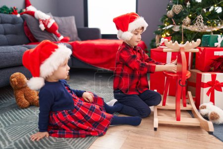 Photo for Adorable boy and girl decorating christmas tree playing with santa claus toy at home - Royalty Free Image