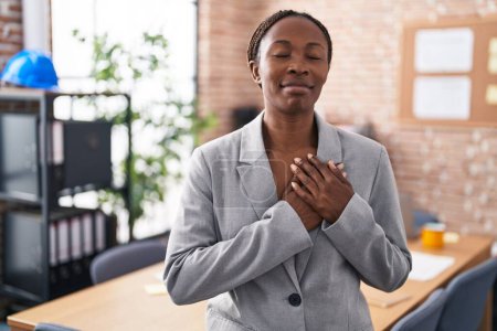 Photo for African american woman at the office smiling with hands on chest with closed eyes and grateful gesture on face. health concept. - Royalty Free Image