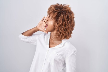 Photo for Young hispanic woman with curly hair standing over white background shouting and screaming loud to side with hand on mouth. communication concept. - Royalty Free Image