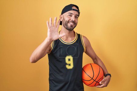 Photo for Middle age bald man holding basketball ball over yellow background waiving saying hello happy and smiling, friendly welcome gesture - Royalty Free Image
