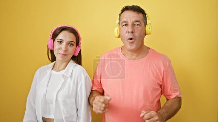 Téléchargez les photos : Père et fille écoutent de la musique et dansent sur fond jaune isolé - en image libre de droit