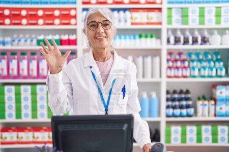 Téléchargez les photos : Femme d'âge moyen avec des tatouages travaillant à la pharmacie pharmacie montrant et pointant vers le haut avec les doigts numéro cinq tout en souriant confiant et heureux. - en image libre de droit