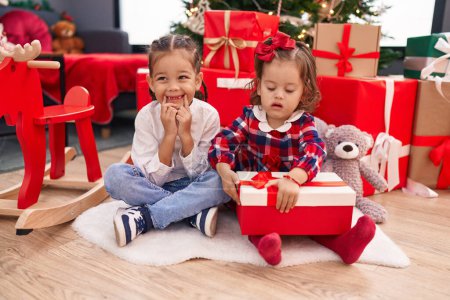 Foto de Hermano y hermana desempacando regalo sentado en el suelo por el árbol de Navidad en casa - Imagen libre de derechos
