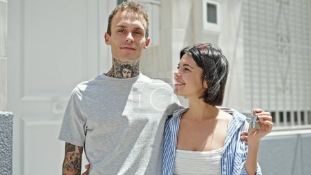 Téléchargez les photos : Beau couple se serrant dans ses bras tenant la clé d'une nouvelle maison dans la rue - en image libre de droit
