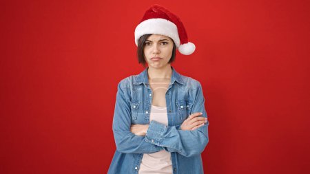 Téléchargez les photos : Jeune femme caucasienne debout contrarié portant chapeau de Noël sur fond rouge isolé - en image libre de droit