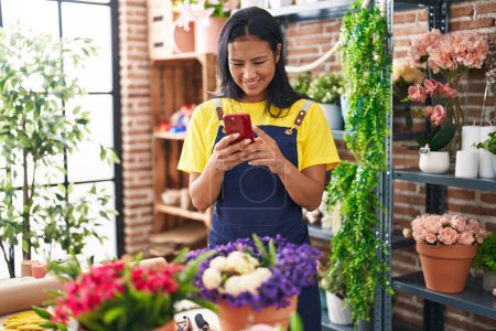 Photo for Young beautiful latin woman florist smiling confident using smartphone at florist - Royalty Free Image